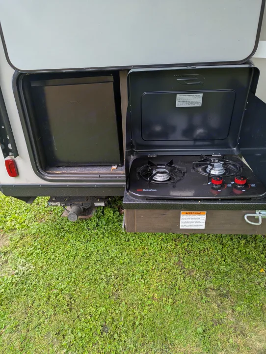 Outdoor kitchen setup on an RV rental, featuring a Hisense mini-fridge and Suburban two-burner stove for camping convenience.. Keystone RV Bullet Crossfire 2020