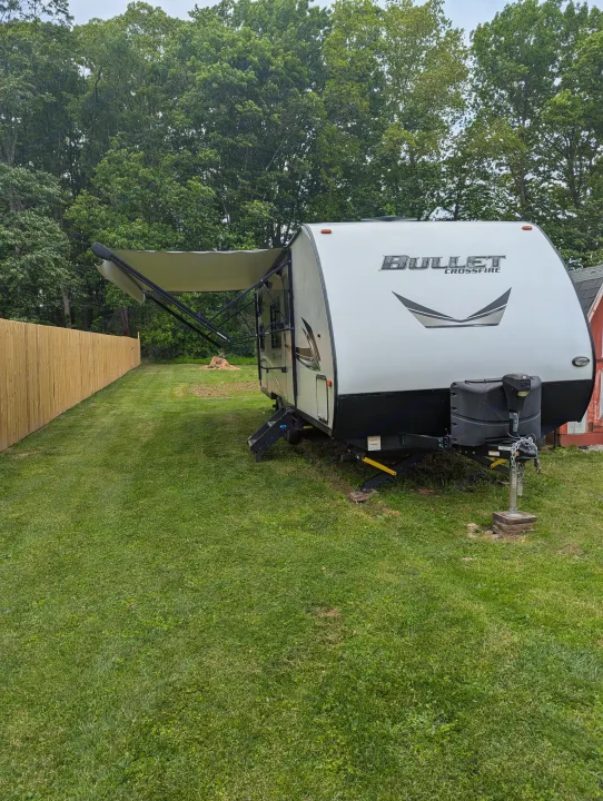 White Bullet Crossfire travel trailer RV rental, awning extended, on a green lawn beside a wooden fence.. Keystone RV Bullet Crossfire 2020