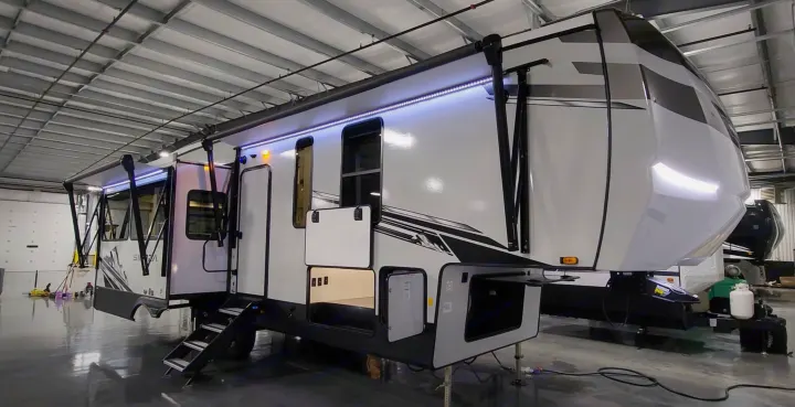 A large white fifth-wheel RV with extended awning and bright LED lighting, perfect for your next rv rental.. Forest River 3370RLS 2024