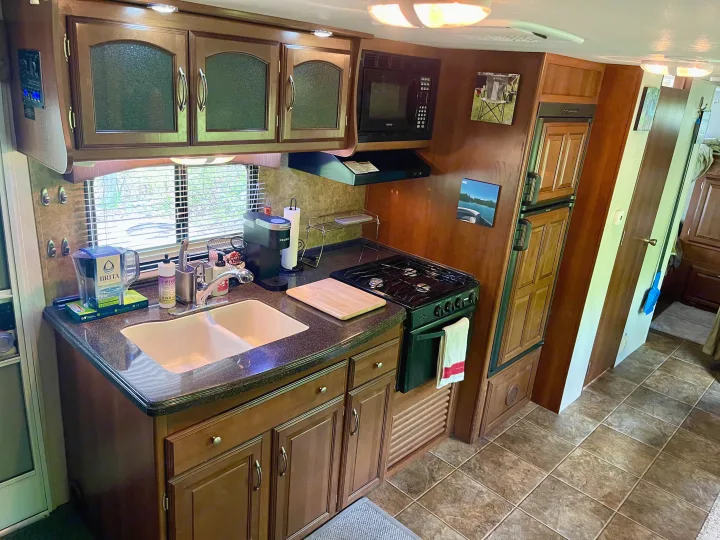 Well-equipped RV rental kitchen featuring a double sink, stove, microwave, fridge, and ample storage for your travels.. Coachmen Freedom Express 2013