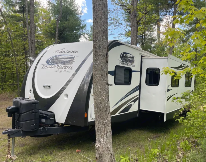 RV rental: a white Coachmen travel trailer with extended slide-out, parked in a wooded campsite among trees.. Coachmen Freedom Express 2013