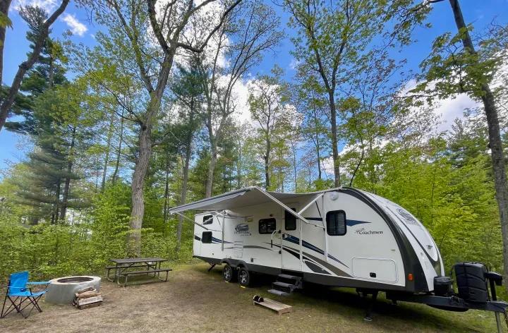 This rv rental campsite features a white travel trailer, fire pit, picnic table, and lush forest scenery.. Coachmen Freedom Express 2013