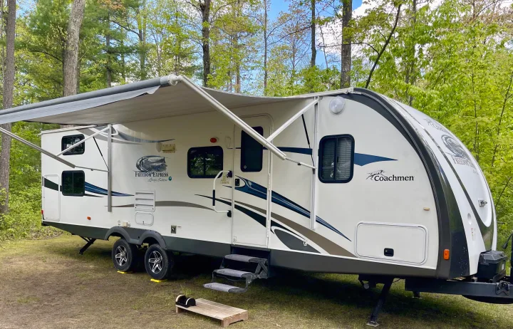 White Coachmen Freedom Express RV rental with awning extended, nestled in a shaded campsite.. Coachmen Freedom Express 2013
