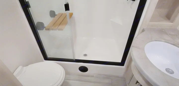 Clean RV rental bathroom featuring a shower with a folding seat, toilet, and modern vanity with sink.. Forest River 3370RLS 2024