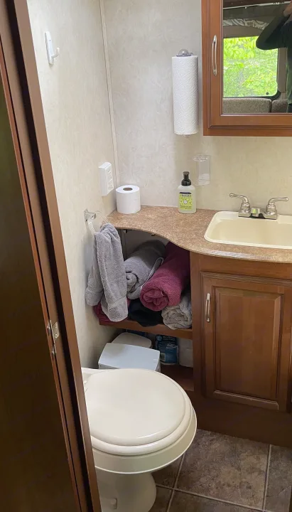RV rental bathroom with toilet, sink, mirror, and compact built-in storage for towels and supplies.. Coachmen Freedom Express 2013