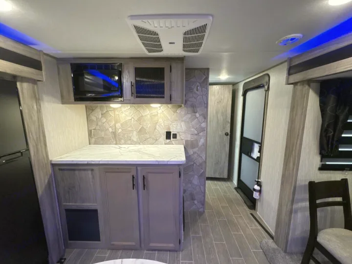RV rental kitchen and living space: modern interior with microwave, stone backsplash, fridge, and blue overhead lighting.. Forest River Cherokee Alpha Wolf 2020