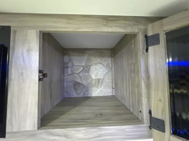 Open cabinet inside an RV rental, featuring a stylish stone-patterned back wall and wood-grain interior for storage.. Forest River Cherokee Alpha Wolf 2020