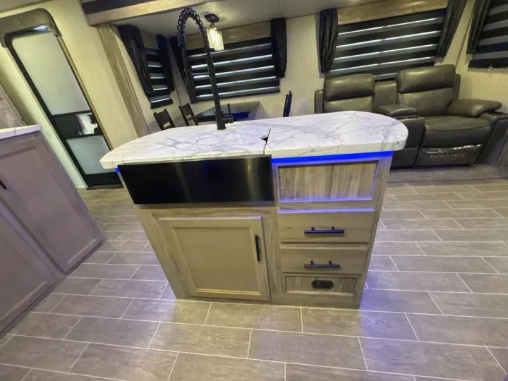 Spacious RV rental interior featuring a modern kitchen island with sink, blue under-lighting, and comfy recliners.. Forest River Cherokee Alpha Wolf 2020