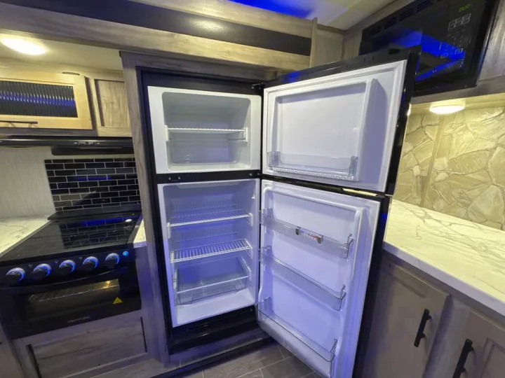 Explore this RV rental's kitchen: open fridge, black stove/oven, black subway tile, and overhead microwave. Ready for trips!. Forest River Cherokee Alpha Wolf 2020