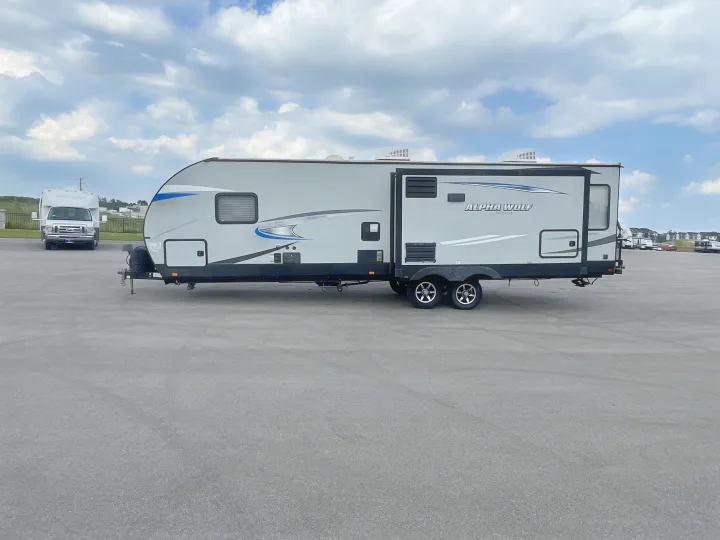 Alpha Wolf travel trailer RV rental, parked on a large asphalt lot. Ready for adventure under a cloudy sky.. Forest River Cherokee Alpha Wolf 2020