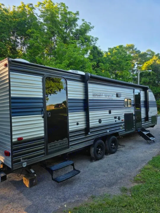 Grey Wolf RV for rv rental, parked on gravel with steps down, surrounded by green trees.. Forest River Cherokee Grey Wolf 2022