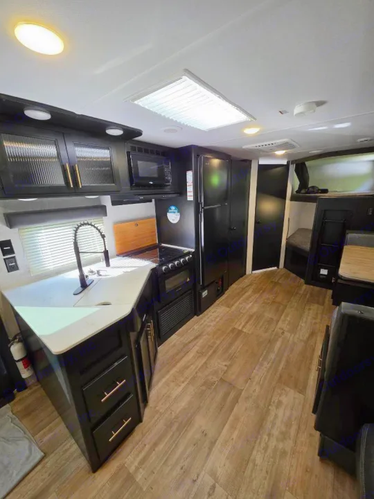 Bright RV rental interior showing a kitchen with dark appliances, light counters, wood floors, and a dinette area.. Forest River Cherokee Grey Wolf 2022