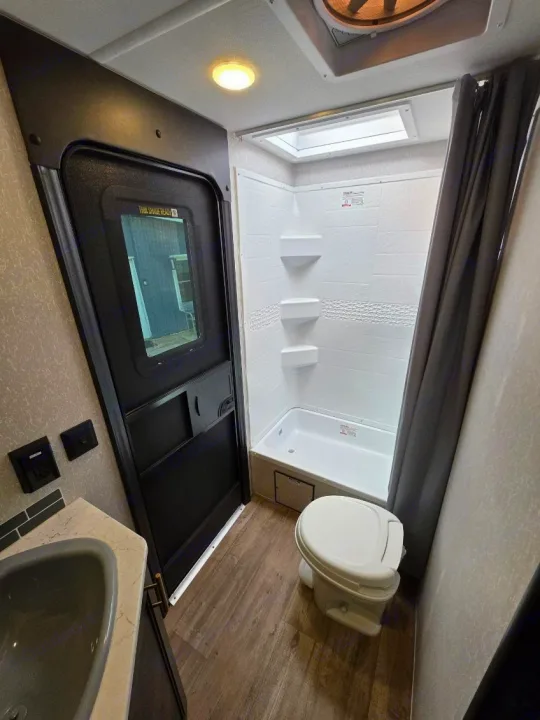 View of a clean and compact RV rental bathroom, equipped with a shower, toilet, and vanity sink.. Forest River Cherokee Grey Wolf 2022