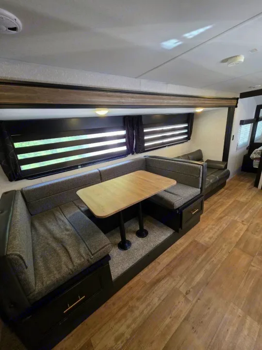 RV rental interior: Grey U-shaped dinette with light wood table, black sofa, and large windows with blinds.. Forest River Cherokee Grey Wolf 2022