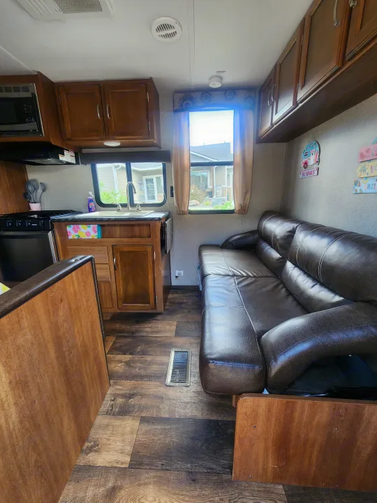 RV rental interior: a functional kitchen area with wooden cabinets and a comfortable living space with a large brown sofa.. Keystone RV Springdale 2018