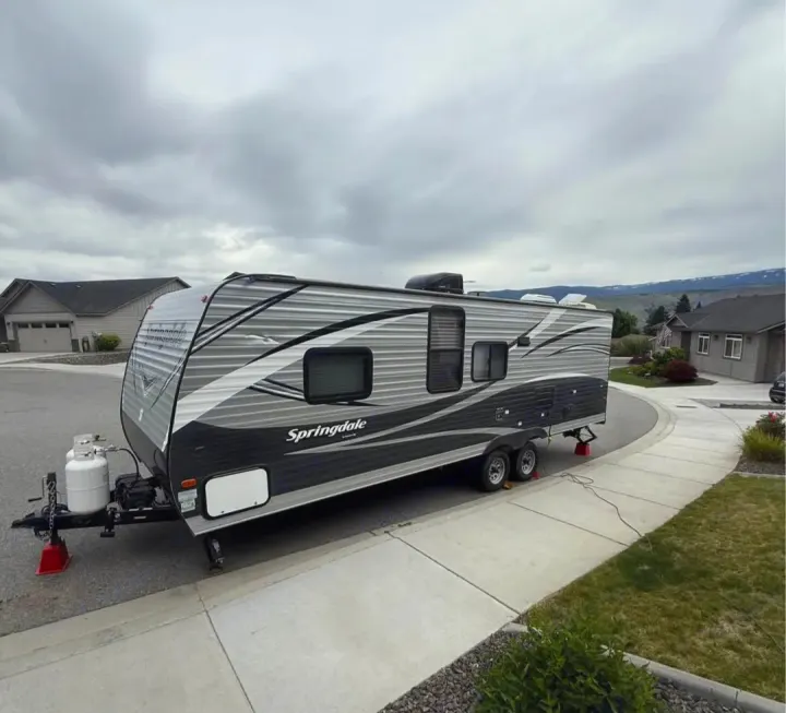 Grey Springdale travel trailer, an RV rental, parked on a suburban street with houses & mountains under a cloudy sky.. Keystone RV Springdale 2018