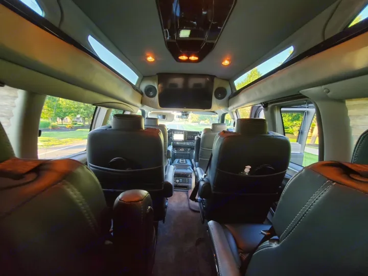 Inside a luxury RV rental: plush black leather seats, an overhead TV, and skylight panels for bright travel.. Chevy Luxury Splinter Express Express Conversion Van 2024