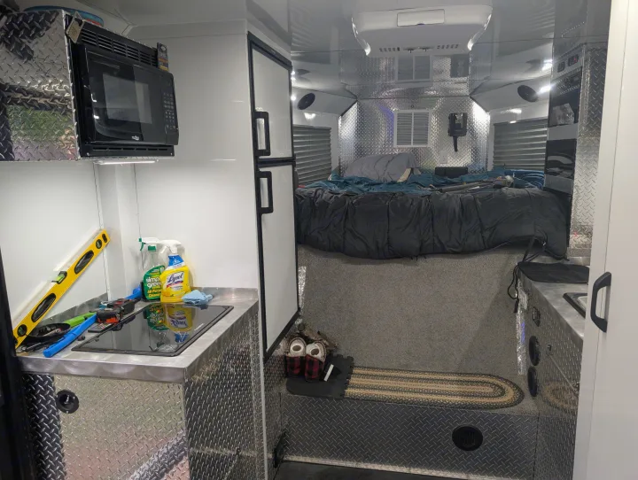 Modern rv rental interior with a compact kitchen, bed area, microwave, fridge, and rugged diamond plate details.. Trails West RPM Toy Hauler 2023