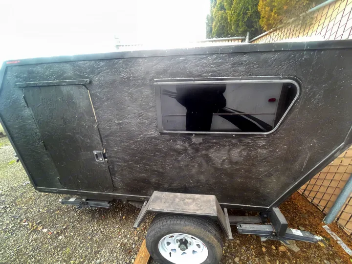 This compact black teardrop trailer, ideal for RV rental, features a side door, window, and textured exterior.. Custom Squaredrop Trailer 2021