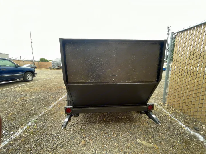 Back of a dark gray utility trailer with red tail lights and stabilizing jacks on a gravel lot near a fence. Suitable for RV rental operations.. Custom Squaredrop Trailer 2021