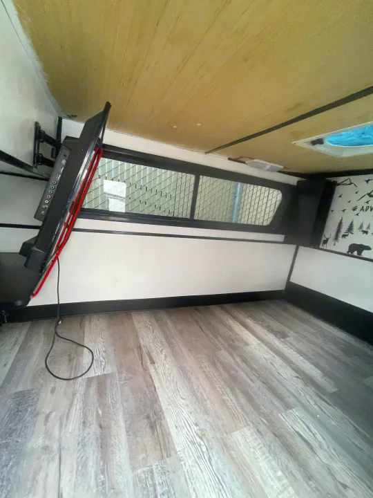 Interior of an RV rental showing a mounted TV, gridded window, wood floor, and adventure wall decals.. Custom Squaredrop Trailer 2021