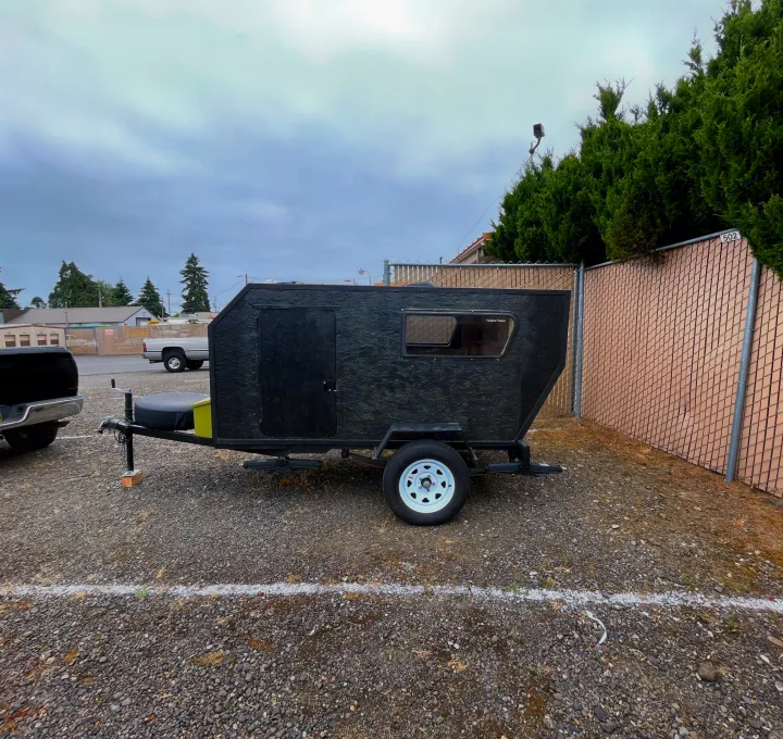 Black 'Teardrop Tom's' camper trailer on a gravel lot, an ideal RV rental for compact adventures.. Custom Squaredrop Trailer 2021