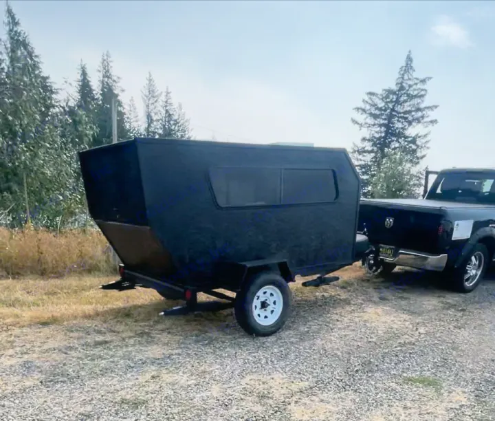 This rugged, black compact RV rental is ready for adventure, hitched to a pickup truck on a gravel lot, with trees in background.. Custom Squaredrop Trailer 2021