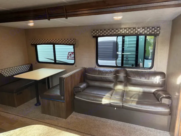 Spacious RV rental living area with a comfortable brown sofa, dining booth, and scenic windows.. Dutchmen Coleman Lantern 2020
