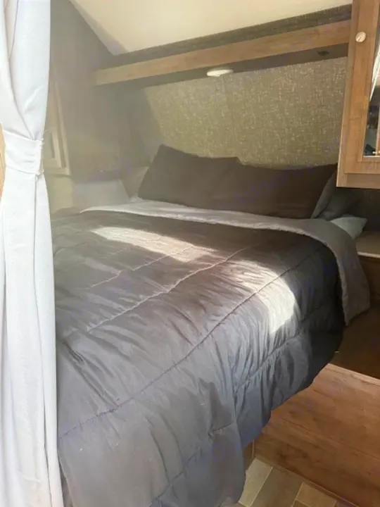 Cozy RV rental bedroom with a large bed, overhead storage, and patterned walls. Perfect for travel.. Dutchmen Coleman Lantern 2020