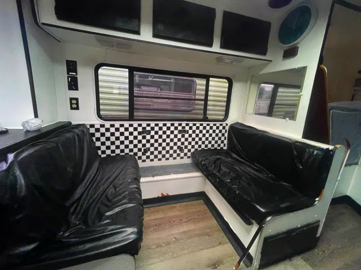 RV rental interior with two black vinyl benches, a checkered wall panel, and windows, offering a travel-ready space.. Skyline Century 1985