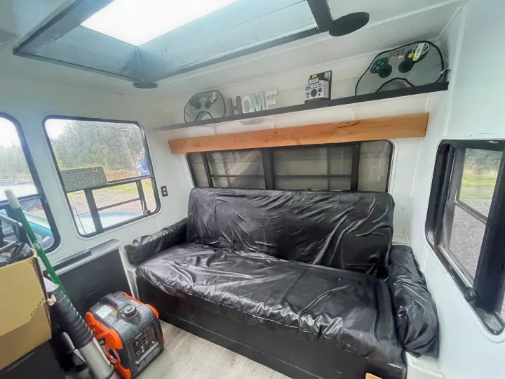 Compact RV rental interior featuring a black futon, overhead skylight, gaming gear, and a portable generator.. Skyline Century 1985