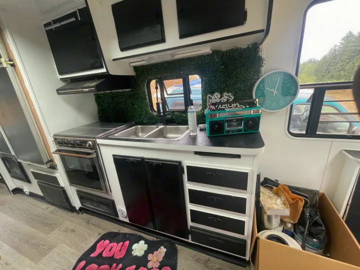 RV rental kitchen: Modern interior with stove, double sink, green wall decor, and teal clock/boombox.. Skyline Century 1985