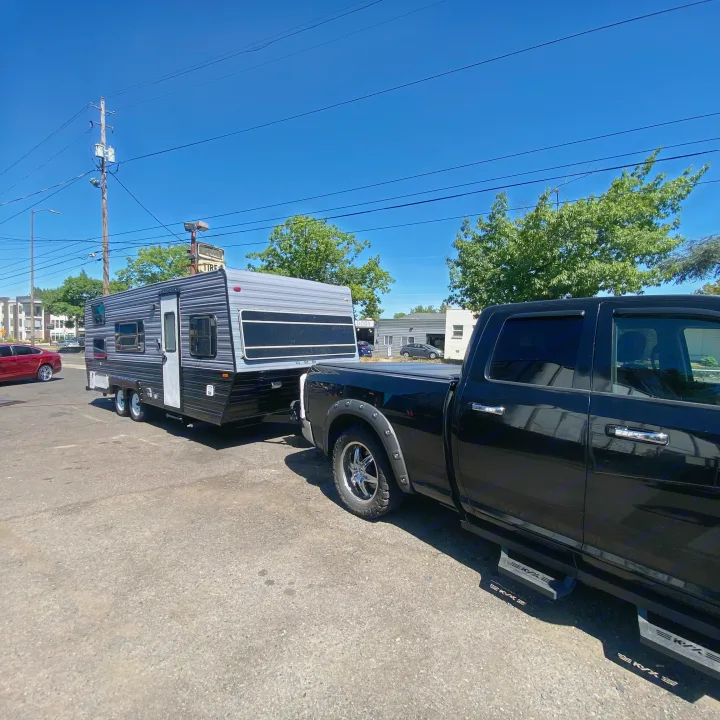 Black pickup truck hitched to a grey and black travel trailer, an RV rental ready for the road.. Skyline Century 1985
