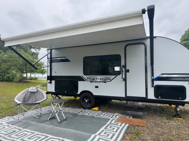 Grey RV rental at a scenic campsite with extended awning, outdoor mat, chair, and table by the water.. Forest River Salem FSX PLATINUM 2021