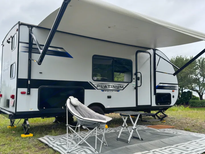 An RV rental showing a travel trailer, fully set up at a grassy campsite with an extended awning, chair, and table.. Forest River Salem FSX PLATINUM 2021