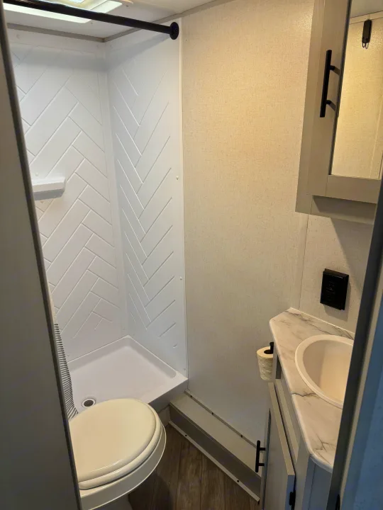 Clean RV rental bathroom interior featuring a white herringbone shower, toilet, and sink vanity.. Forest River Salem FSX PLATINUM 2021
