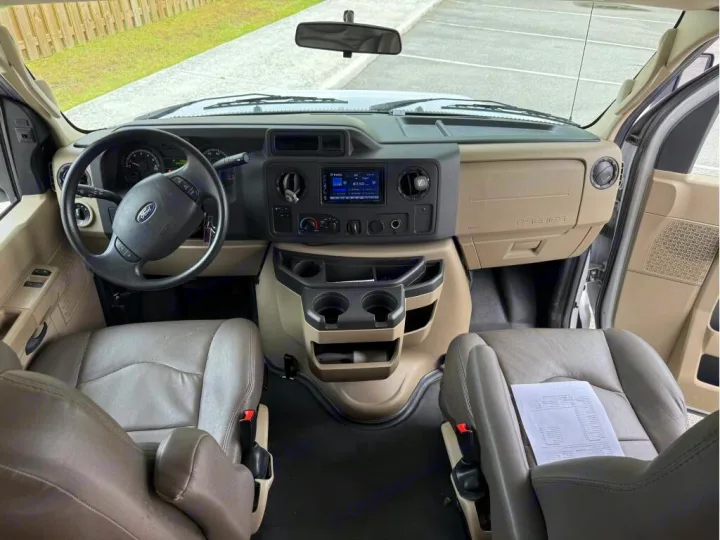 Step inside this RV rental! The beige dashboard, Ford steering wheel, and two front seats are visible, ready for your adventure.. Entegra Coach Odyssey 2020