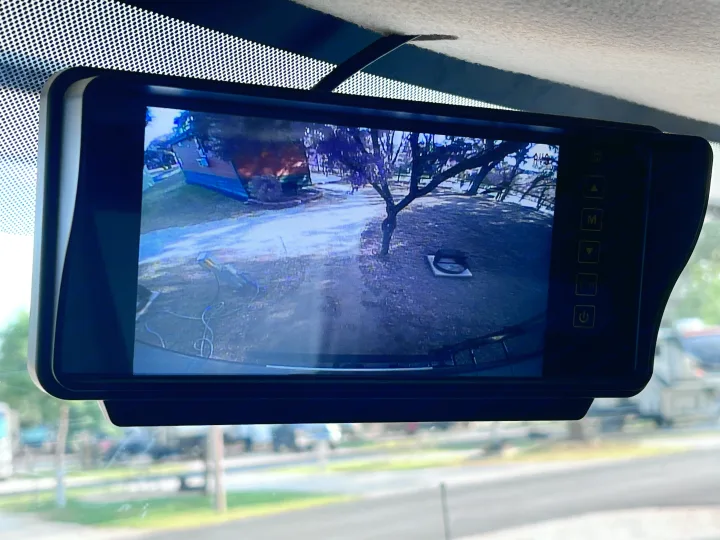 RV rental backup camera monitor displays a campsite view, showing a path, trees, and a utility hookup.. East to West Entrada 2025