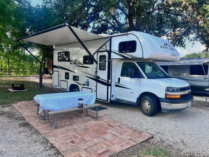RV rental: East to West Entrada Class C camper at a wooded campsite with awning, picnic table, and fire pit.. East to West Entrada 2025
