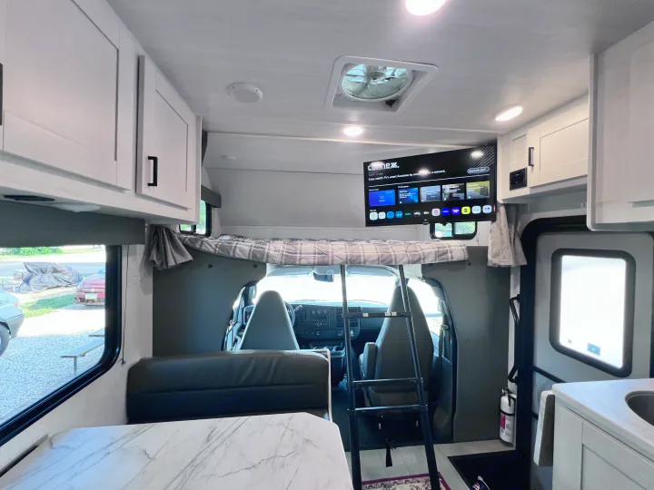 RV rental interior featuring an overhead bed, smart TV, kitchen, and dining area for compact travel comfort.. East to West Entrada 2025