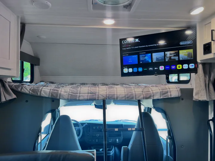 RV rental interior: over-cab bunk bed, smart TV powered by webOS Hub, and the vehicle's driver's cab.. East to West Entrada 2025