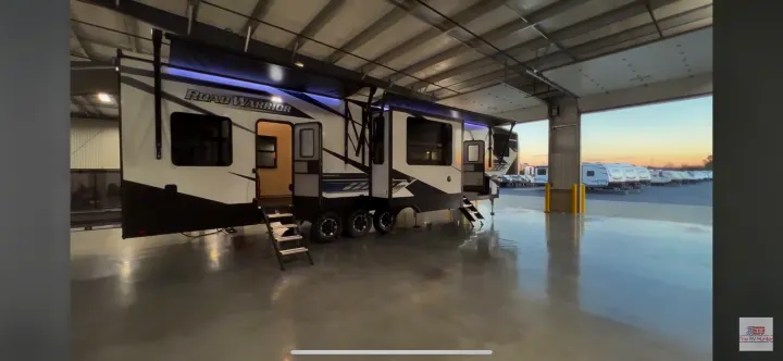 Sleek "ROAD WARRIOR" toy hauler RV for rent, shown indoors with steps extended. Rows of RVs outside.. Heartland RVs Road Warrior Toy Hauler 2022