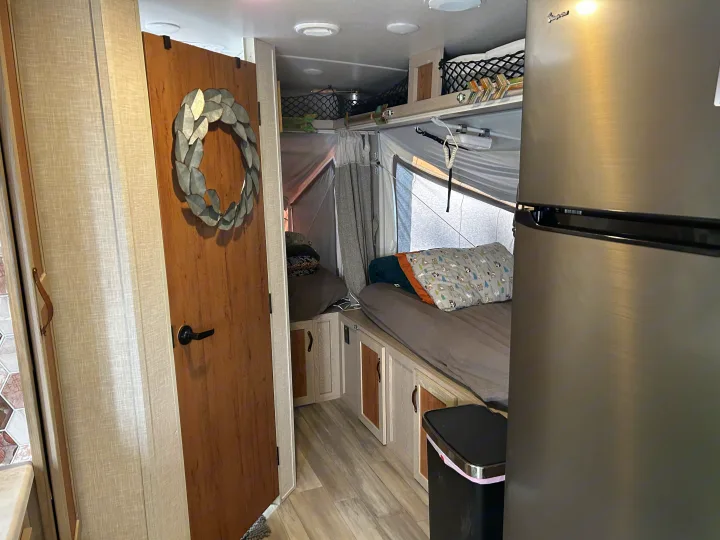 RV rental interior: cozy pop-out bed, built-in storage, and a large stainless steel refrigerator.. Forest River Flagstaff Shamrock 2022