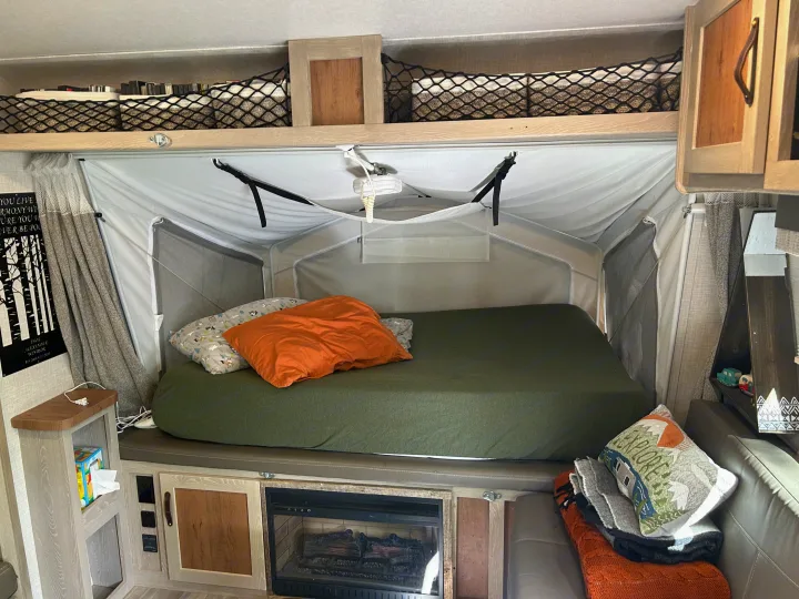 Inside an RV rental: a comfy pop-up bed, overhead storage, and a warm fireplace create a cozy home on wheels.. Forest River Flagstaff Shamrock 2022