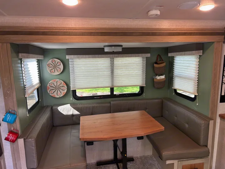 This RV rental features a cozy U-shaped dinette with grey seating, an adjustable wood table, windows with blinds, and green walls.. Forest River Flagstaff Shamrock 2022
