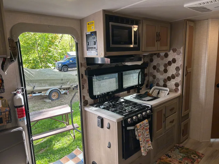 RV rental kitchen: a compact cooking area with a stove, microwave, and sink, overlooking a truck and boat outside.. Forest River Flagstaff Shamrock 2022