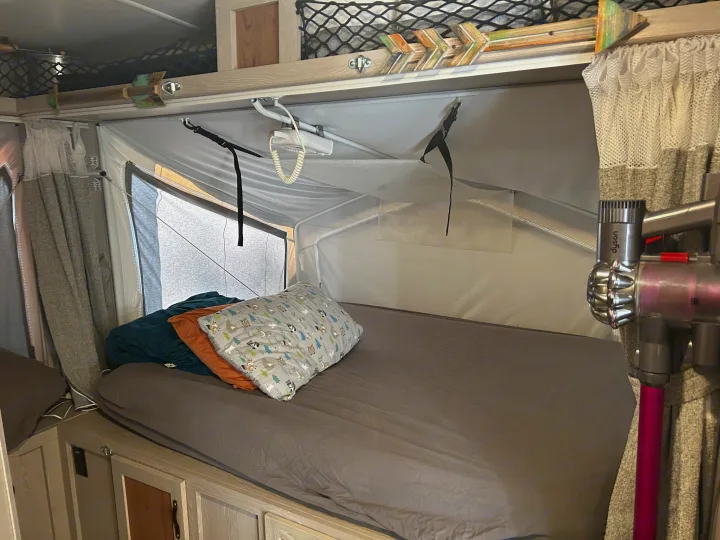 Inside this RV rental pop-up camper: a cozy sleeping area with bed, storage, and Dyson vacuum.. Forest River Flagstaff Shamrock 2022