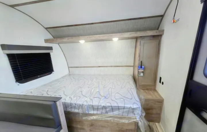 Explore this RV rental's bedroom featuring a bed with a protective plastic cover, window, lighting, and storage cabinet.. Gulf Stream Kingsport Lite 199DD 2025