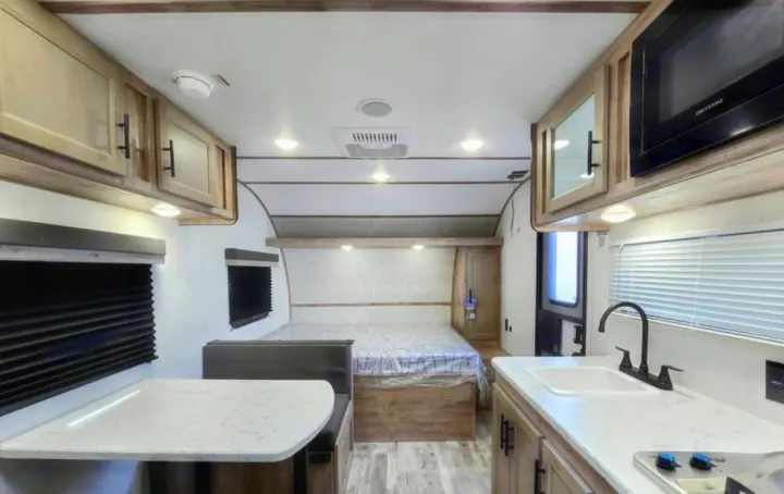 Modern RV rental interior featuring a bright kitchen with a microwave & sink, a dining booth, and a cozy bed area.. Gulf Stream Kingsport Lite 199DD 2025