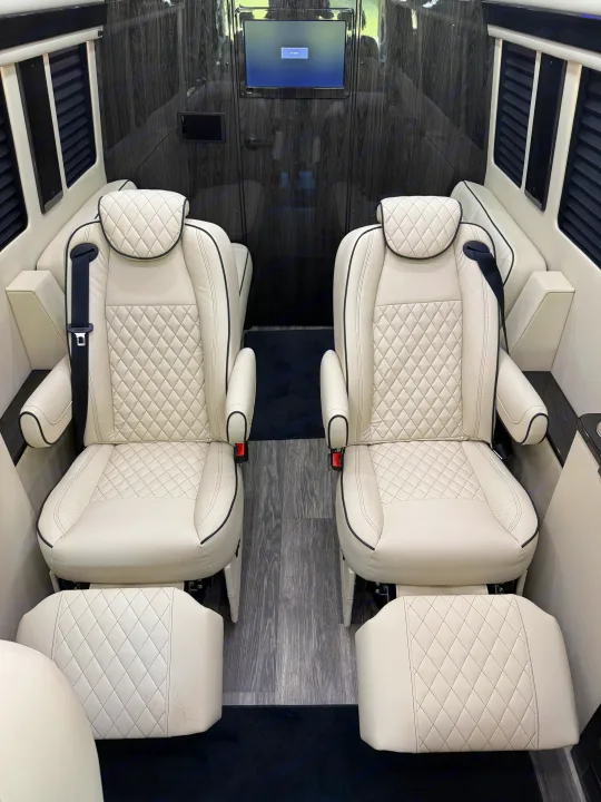 Experience luxury: RV rental interior with two plush cream quilted leather seats, wood paneling, and an entertainment screen.. Mercedes-Benz Sprinter 2025